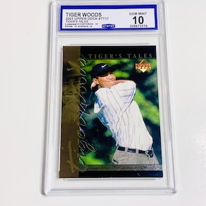 May include: A Tiger Woods 2001 Upper Deck #TT17 trading card, graded Gem Mint 10. The card features a photo of Tiger Woods in action, with the text "TIGER'S TALES" and "Tiger edges Sergio for PGA title - 8/15/99". The card is encased in a protective holder.