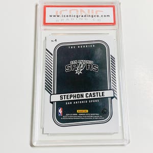 May include: A graded Stephon Castle San Antonio Spurs basketball card. The card is encased in a clear plastic holder with a red and white label from Iconic Grading Co. The card features the Spurs logo and the Panini logo.