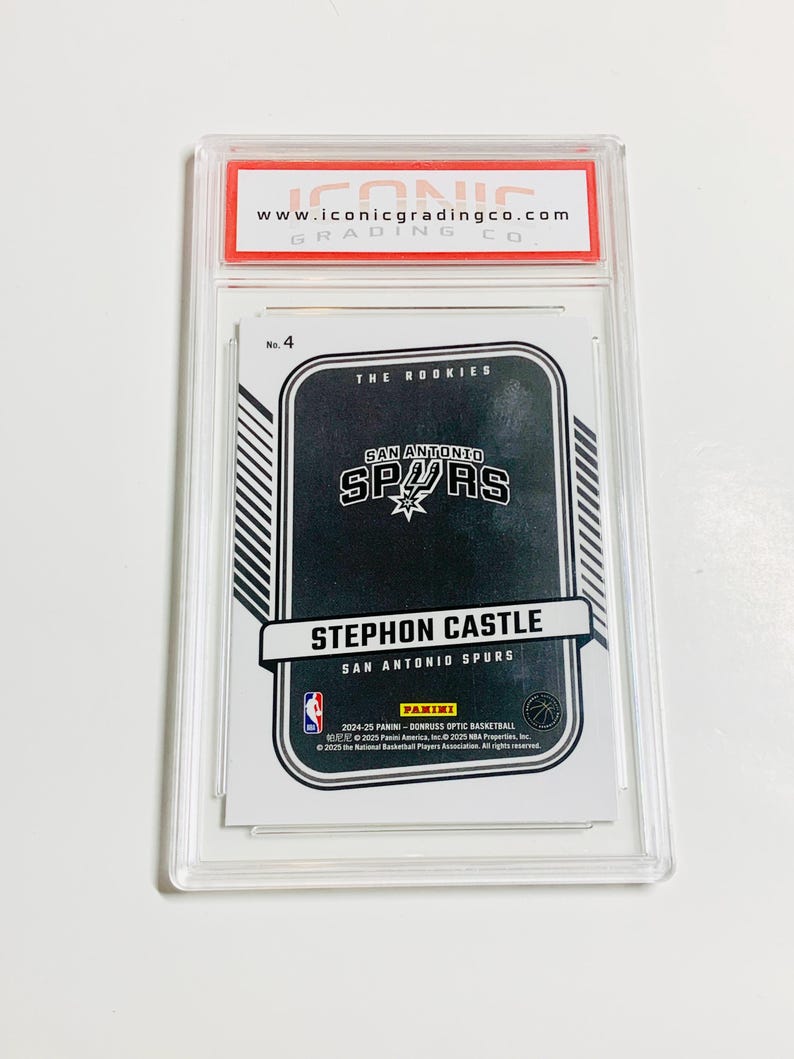 May include: A graded Stephon Castle San Antonio Spurs basketball card. The card is encased in a clear plastic holder with a red and white label from Iconic Grading Co. The card features the Spurs logo and the Panini logo.