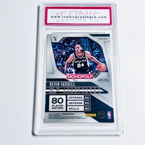 K&ouml;nnte beinhalten: Eine Basketball-Sammelkarte in einer transparenten Kunststoffh&uuml;lle. Die Karte zeigt Devin Vassell von den Spurs, mit Spielerstatistiken und einem "Monopoly"-Logo. Die Karte wird von Iconic Grading Co. bewertet.