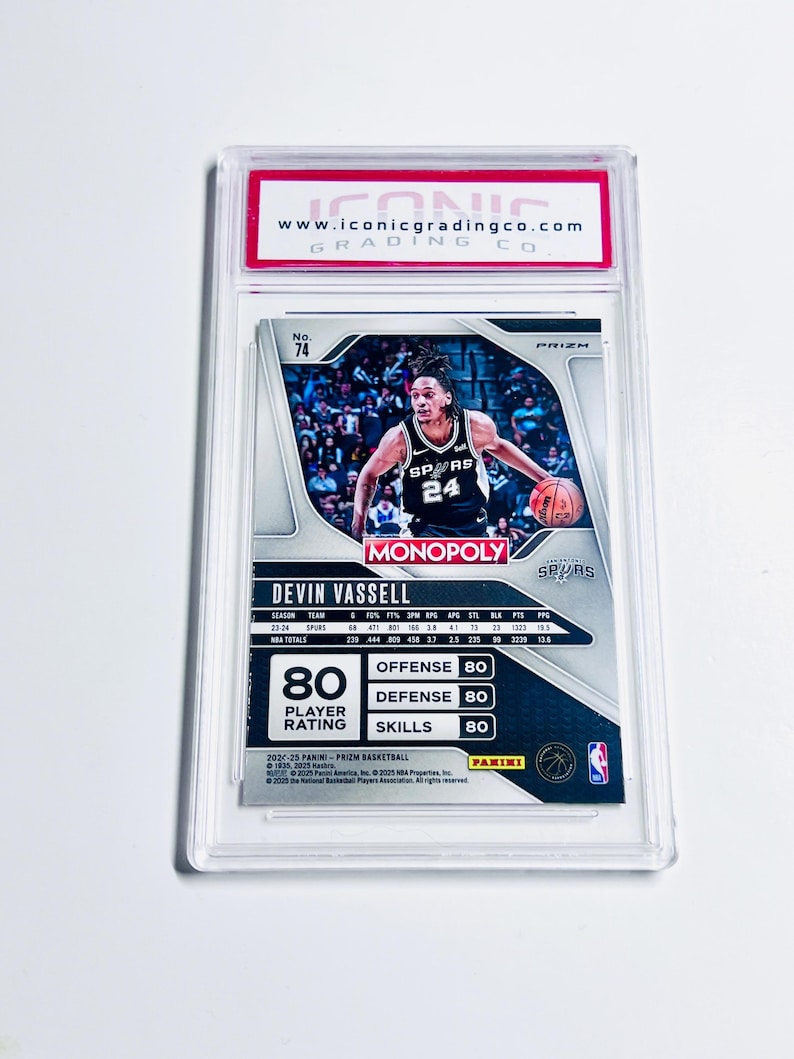 K&ouml;nnte beinhalten: Eine Basketball-Sammelkarte in einer transparenten Kunststoffh&uuml;lle. Die Karte zeigt Devin Vassell von den Spurs, mit Spielerstatistiken und einem "Monopoly"-Logo. Die Karte wird von Iconic Grading Co. bewertet.