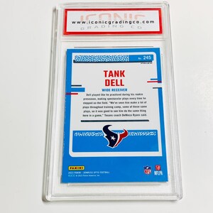 May include: A Tank Dell football trading card, graded and encased in a clear plastic holder. The card features a blue background with the player's name and team logo. The card is from the 2023 Panini Donruss Optic Football series.