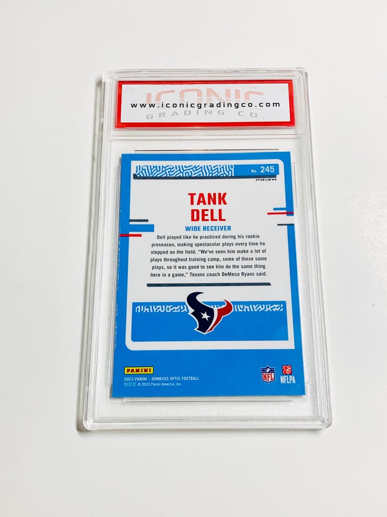May include: A Tank Dell football trading card, graded and encased in a clear plastic holder. The card features a blue background with the player's name and team logo. The card is from the 2023 Panini Donruss Optic Football series.