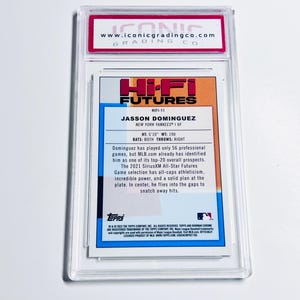 May include: A baseball card of Jasson Dominguez, a New York Yankees player, from the Hi-Fi Futures series. The card is encased in a clear plastic holder with a red and white label from Iconic Grading Co. The card's back features player stats and a description.