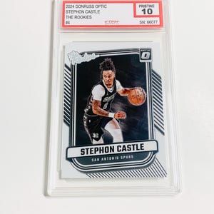 May include: A basketball trading card featuring Stephon Castle of the San Antonio Spurs. The card is graded Pristine 10 and is from the 2024 Donruss Optic set. The card is encased in a clear protective holder.