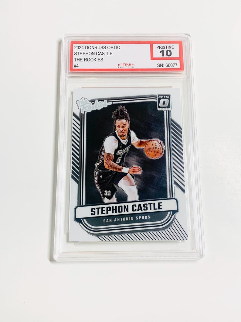 May include: A basketball trading card featuring Stephon Castle of the San Antonio Spurs. The card is graded Pristine 10 and is from the 2024 Donruss Optic set. The card is encased in a clear protective holder.