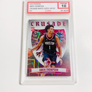 May include: A basketball trading card featuring Amen Thompson in a Houston Rockets uniform. The card is graded Pristine 10 and includes the text "CRUSADE" and "2023 PHOENIX". The card is encased in a clear protective holder.