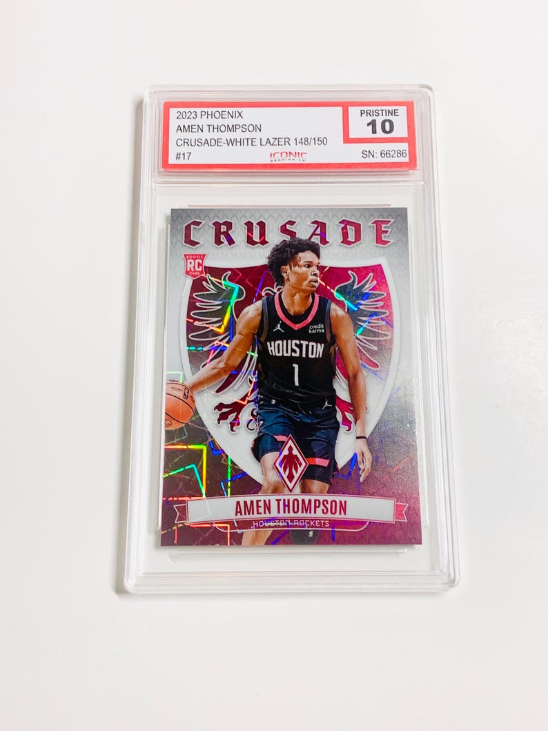 May include: A basketball trading card featuring Amen Thompson in a Houston Rockets uniform. The card is graded Pristine 10 and includes the text "CRUSADE" and "2023 PHOENIX". The card is encased in a clear protective holder.
