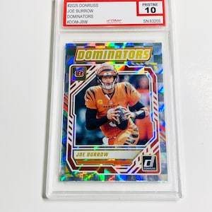 Może przedstawiać: Karta do gry w futbol amerykański Joe Burrow z serii Donruss Dominators, oceniona na Pristine 10. Karta przedstawia zdjęcie Burrowa w jego mundurze Bengals, trzymającego piłkę do futbolu. Karta jest zamknięta w ochronnym uchwycie.
