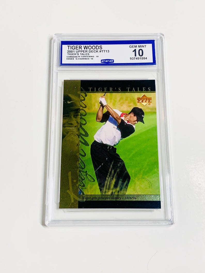 Op de afbeelding: Een Tiger Woods 2001 Upper Deck #TT13 trading card, beoordeeld als GEM MINT 10, in een beschermende houder. De kaart toont Tiger Woods die golf speelt en de tekst "TIGER'S TALES".