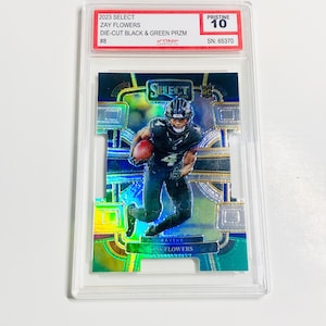 May include: A Zay Flowers football trading card from the 2023 Select series. The card features a die-cut design with black and green prism colors. The card is graded Pristine 10 and encased in a protective holder.