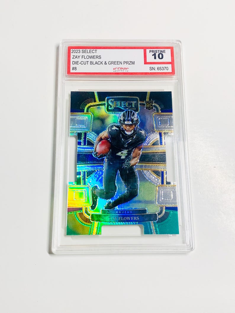 May include: A Zay Flowers football trading card from the 2023 Select series. The card features a die-cut design with black and green prism colors. The card is graded Pristine 10 and encased in a protective holder.