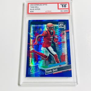 May include: A Tank Dell football card from the 2023 Donruss Optic series, Blue Hyper edition, graded Pristine 10. The card features a player in a red uniform. The card is encased in a clear protective holder.