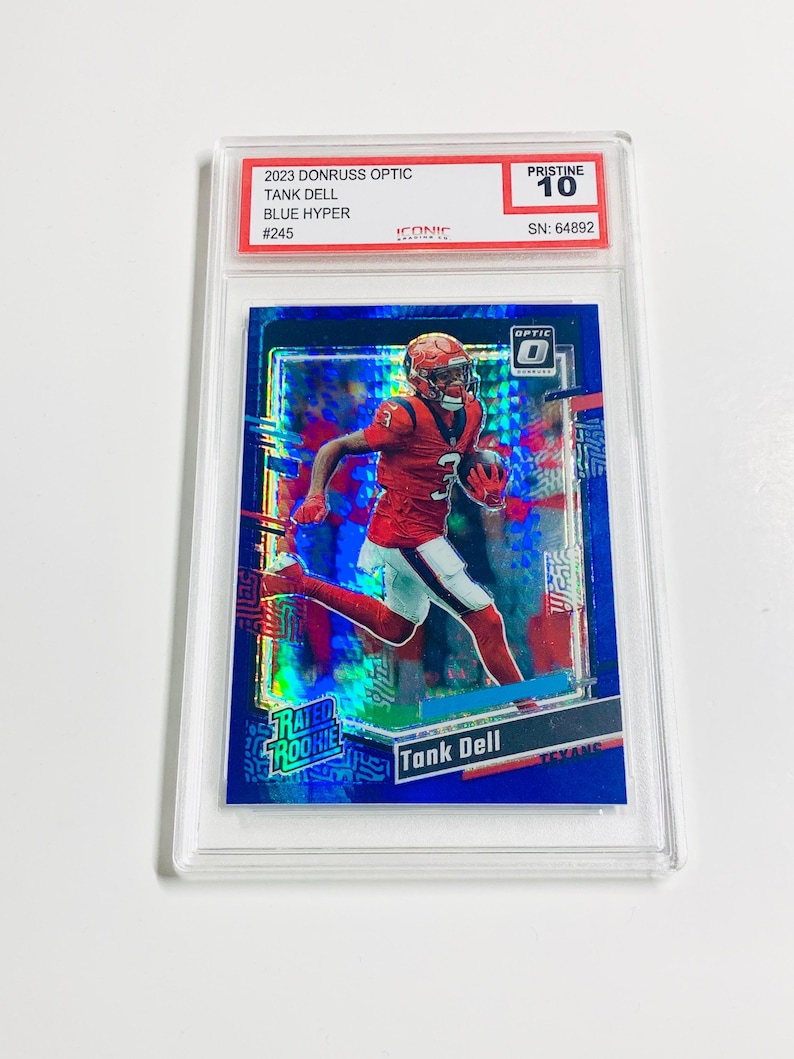 May include: A Tank Dell football card from the 2023 Donruss Optic series, Blue Hyper edition, graded Pristine 10. The card features a player in a red uniform. The card is encased in a clear protective holder.