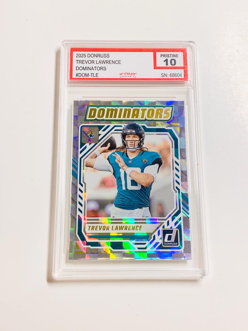 Op de afbeelding: Een 2025 Donruss Trevor Lawrence Dominators verzamelkaart, beoordeeld als Pristine 10, in een beschermende houder. De kaart toont Trevor Lawrence in een teal en zwart uniform. Het woord "Dominators" staat in grote, vette letters.