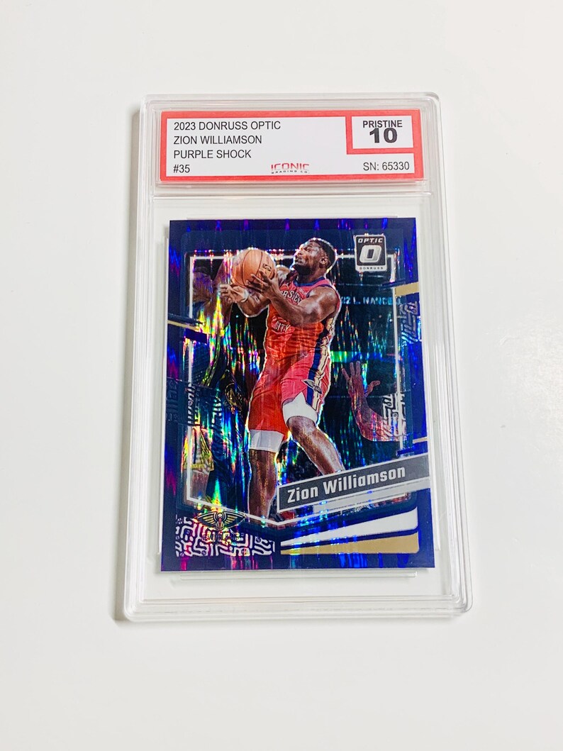 Pu&ograve; includere: Una carta collezionabile di basket con Zion Williamson in uniforme rossa e bianca, che tiene un pallone da basket. La carta &egrave; racchiusa in un supporto di plastica trasparente. Il testo sulla carta include "2023 Donruss Optic", "Purple Shock" e "Pristine 10."