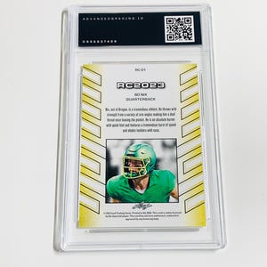 K&ouml;nnte beinhalten: Eine bewertete RC2023 Bo Nix Quarterback Trading Card. Die Karte zeigt ein Foto des Spielers in einem gr&uuml;nen Helm und Uniform. Die Karte ist in einem transparenten Kunststoffhalter mit dem Text "ADVANCEDGRADING.IO" oben eingeschlossen.