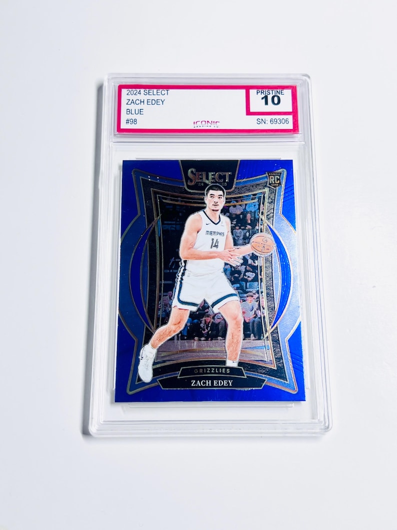 May include: A blue basketball trading card featuring Zach Edey in a Grizzlies uniform. The card is graded Pristine 10 and encased in a clear protective holder. The card's details include "2024 Select," "Zach Edey," and "#98."