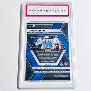 May include: A graded Justin Herbert Los Angeles Chargers football card. The card features a blue and silver mosaic design with player stats and the Panini Prizm logo. The card is encased in a clear protective holder.