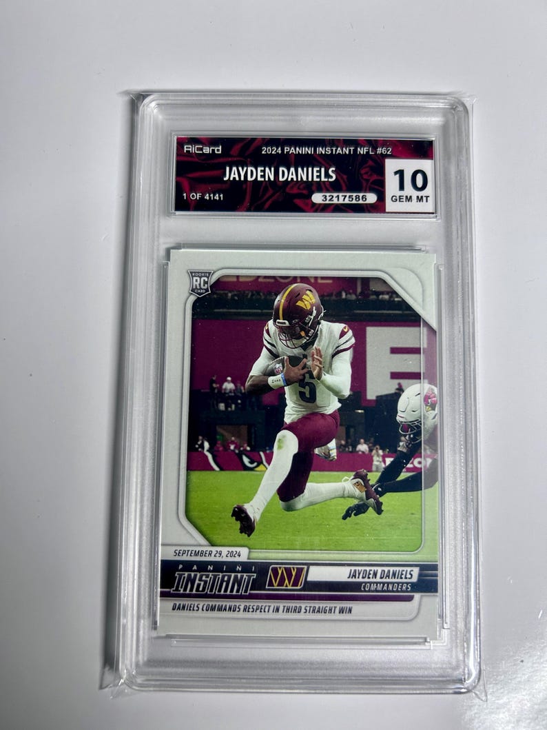 Puede incluir: Una tarjeta comercial de 2024 Panini Instant NFL #62 calificada con Jayden Daniels de los Commanders. La tarjeta est&aacute; calificada como 10 GEM MT y est&aacute; encerrada en un soporte protector. La tarjeta muestra a Daniels en acci&oacute;n, con el texto "DANIELS COMMANDS RESPECT IN THIRD STRAIGHT WIN".