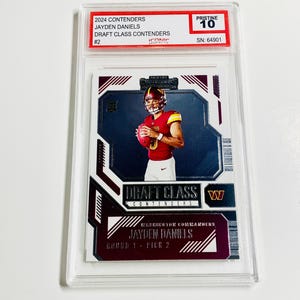 May include: A football trading card featuring Jayden Daniels of the Washington Commanders, encased in a protective holder. The card displays "2024 Contenders" and "Draft Class Contenders" text. It is graded "Pristine 10".