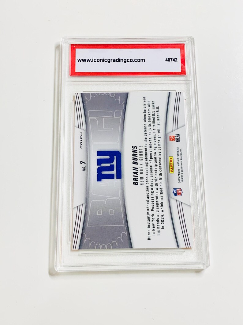 Puede incluir: Una tarjeta comercial calificada de Brian Burns, jugador de los New York Giants, dentro de un soporte de pl&aacute;stico transparente. La tarjeta muestra el logotipo de los Giants y la informaci&oacute;n del jugador. La parte superior del soporte tiene una etiqueta roja con una direcci&oacute;n web.