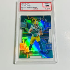 May include: A football trading card featuring Tucker Kraft in a green and yellow Packers uniform. The card is graded Pristine 10 and includes the text "2023 Select" and "Die-Cut Blk & Grn Prizm".