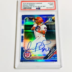 Op de afbeelding: Een honkbalkaart met Israel Pineda in een Washington Nationals-uniform. De kaart zit in een beschermende houder en heeft de tekst "2019 Bowman Chrome" en "Prospects Auto-Blue Ref.". De kaart is beoordeeld als Mint 9.