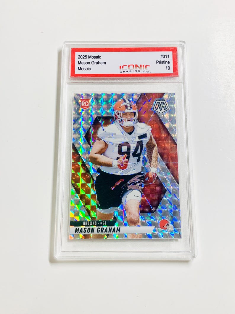 Op de afbeelding: Een 2025 Mosaic voetbal trading card met Mason Graham van de Browns, beoordeeld als Pristine 10. De kaart heeft een moza&iuml;ekontwerp met een speler afbeelding in een wit uniform en het nummer 94. De kaart zit in een doorzichtige beschermhoes.