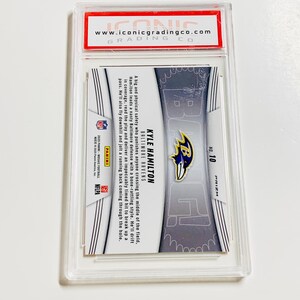 May include: A Kyle Hamilton Baltimore Ravens football card in a protective case. The card features a player image, team logo, and the number 10. The card is from the Prizm series and includes text about the player.
