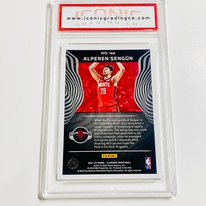 Puede incluir: Una tarjeta de baloncesto de Alperen Sengun calificada de la serie Panini Illusions 2021-22. La tarjeta presenta una foto de Sengun con una camiseta roja de los Rockets. La tarjeta est&aacute; dentro de un soporte de pl&aacute;stico transparente con el logotipo de Iconic Grading Co.
