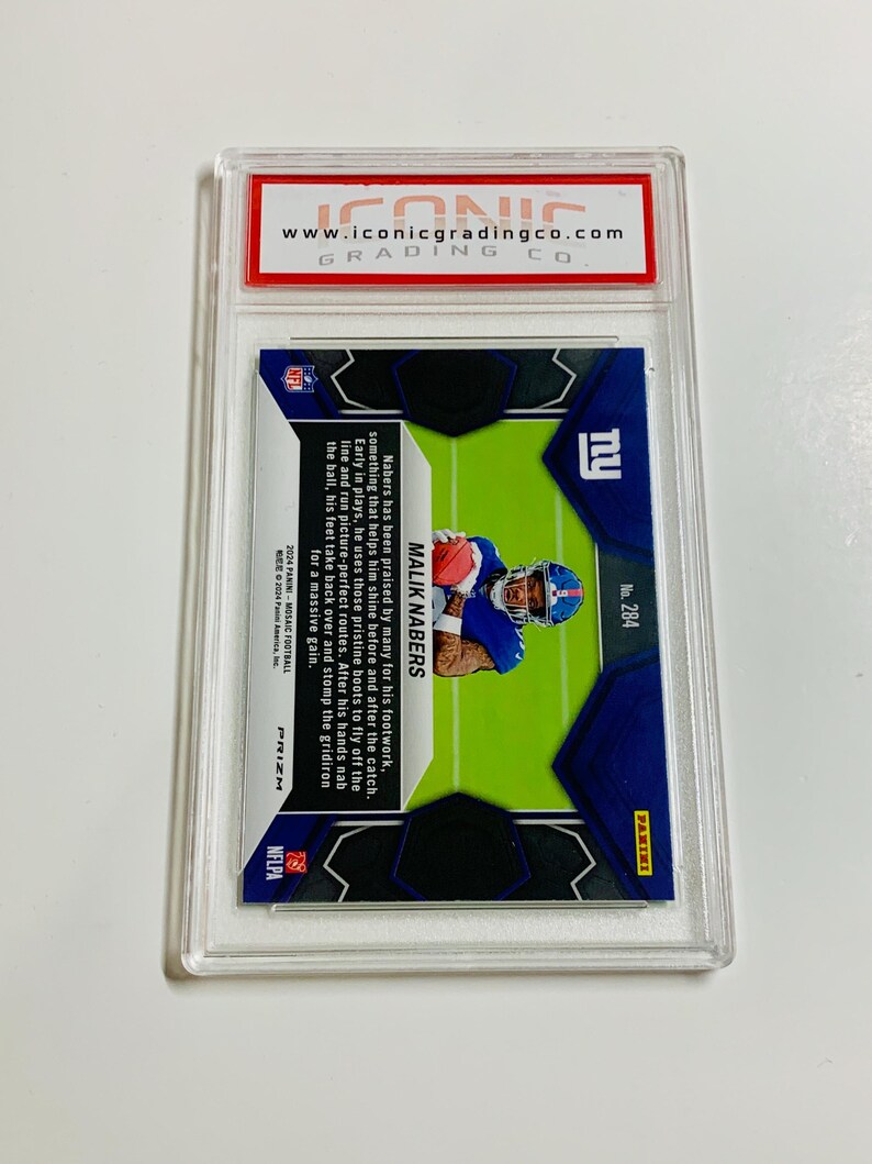 K&ouml;nnte beinhalten: Eine Football-Sammelkarte in einer transparenten Kunststoffh&uuml;lle. Die Karte zeigt einen Spieler in blauem Trikot mit dem Namen "MALIK NABERS". Die Karte ist mit "PRIZM" und "NFLPA" gekennzeichnet. Oben auf der H&uuml;lle befindet sich ein rot-wei&szlig;es Etikett mit "www.iconicgradingco.com".