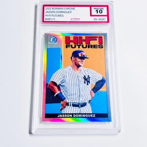 May include: A baseball card featuring Jasson Dominguez in a New York Yankees uniform. The card is from the 2022 Bowman Chrome Hi-Fi Futures series and is graded Pristine 10. The card is encased in a clear protective holder.
