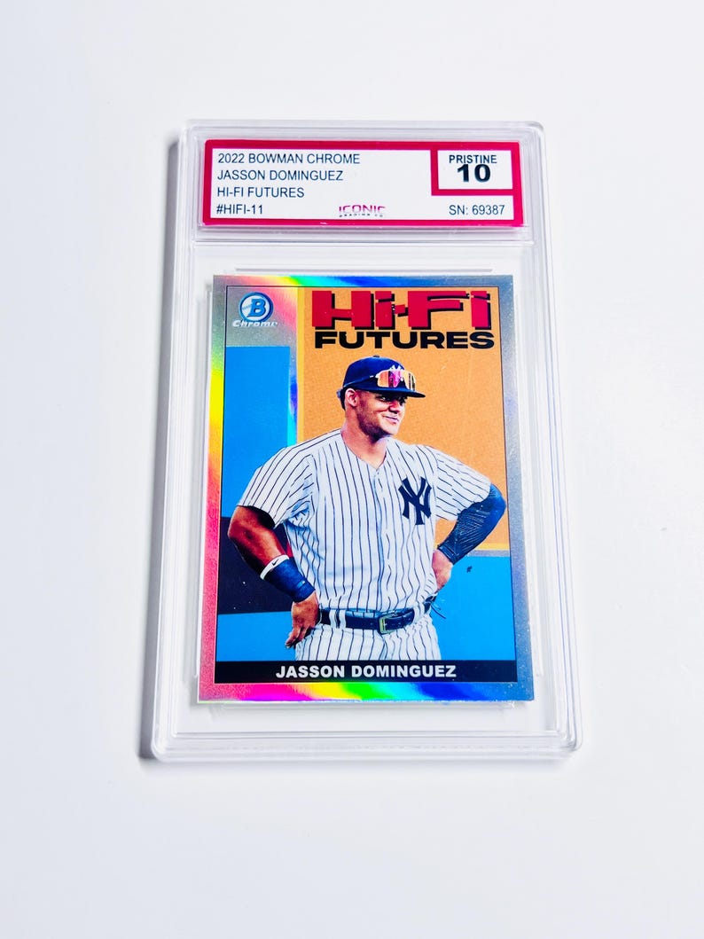 May include: A baseball card featuring Jasson Dominguez in a New York Yankees uniform. The card is from the 2022 Bowman Chrome Hi-Fi Futures series and is graded Pristine 10. The card is encased in a clear protective holder.