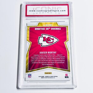 May include: A Panini football trading card featuring Xavier Worthy, drafted 28th overall. The card has a red and gold design with the Kansas City Chiefs logo. The card is encased in a clear protective holder.