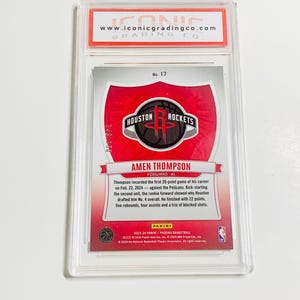May include: A basketball trading card featuring Amen Thompson of the Houston Rockets, graded by Iconic Grading Co. The card has a red and white design with the Rockets logo and player information. The card is encased in a clear protective holder.