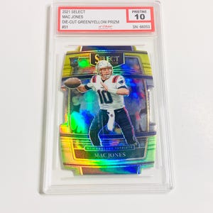 May include: A graded 2021 Select Mac Jones football card. The card features a die-cut green and yellow Prizm design with the player in action. The card is graded Pristine 10 and includes the serial number 66053.
