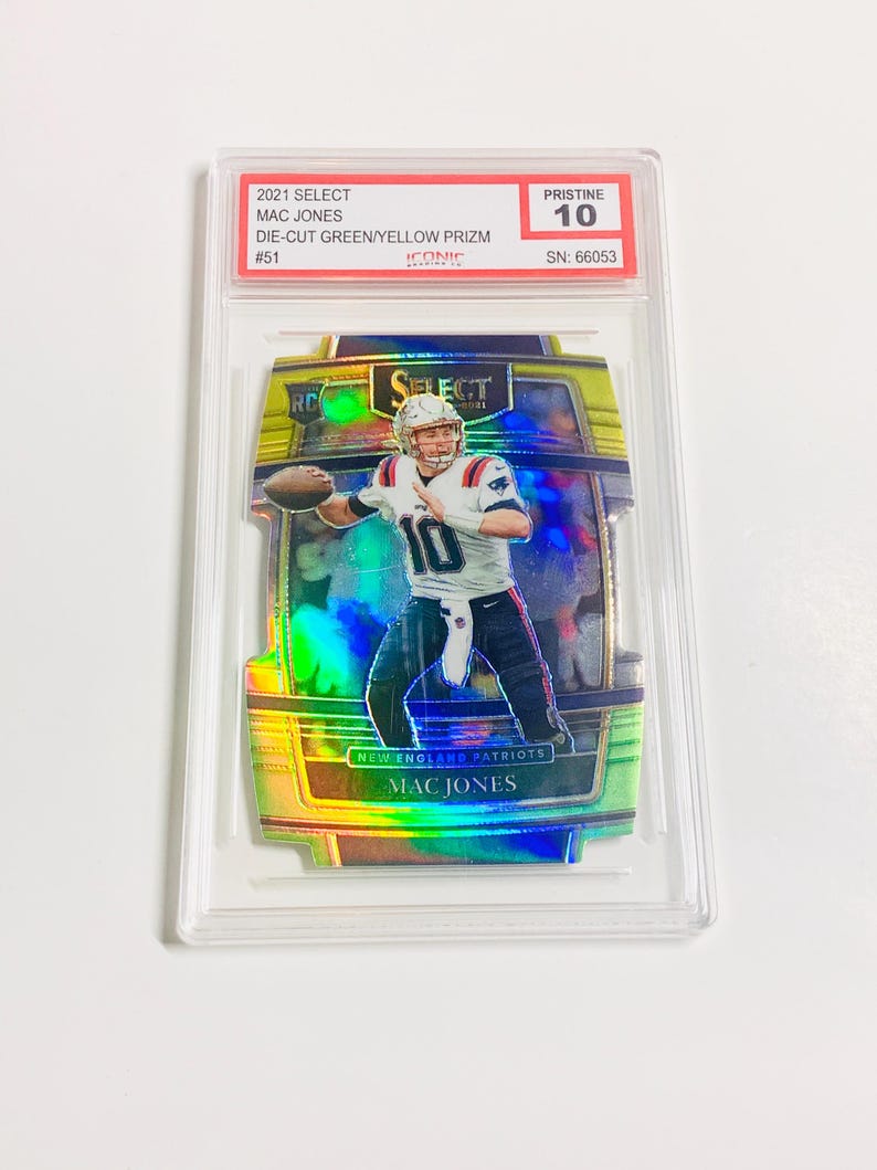 May include: A graded 2021 Select Mac Jones football card. The card features a die-cut green and yellow Prizm design with the player in action. The card is graded Pristine 10 and includes the serial number 66053.