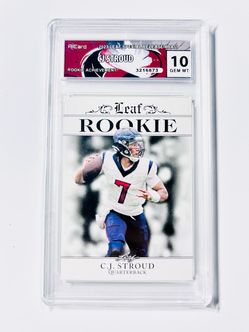 Puede incluir: Una tarjeta coleccionable deportiva calificada con C.J. Stroud, un mariscal de campo, con uniforme blanco y azul. La tarjeta est&aacute; etiquetada como "Rookie" e incluye el texto "2023 Leaf Special Release". La tarjeta est&aacute; calificada con un 10, GEM MT. La tarjeta est&aacute; dentro de un soporte de pl&aacute;stico transparente.