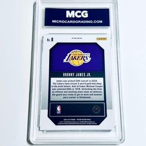 May include: A basketball trading card encased in a clear protective holder. The card features the Los Angeles Lakers logo and text that reads "BRONNY JAMES JR." The top of the holder has the text "MCG MICROCARDGRADING.COM".