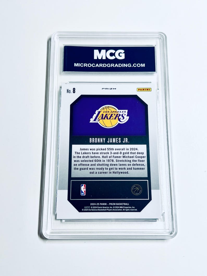 May include: A basketball trading card encased in a clear protective holder. The card features the Los Angeles Lakers logo and text that reads "BRONNY JAMES JR." The top of the holder has the text "MCG MICROCARDGRADING.COM".