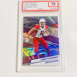 May include: A graded trading card featuring Larry Fitzgerald in a red and white uniform. The card is labeled "2025 Revolution" and "Blue Swirl 87/99". The card is encased in a clear protective holder and graded "Pristine 10".