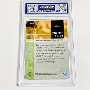 May include: A Tiger Woods trading card encased in a clear plastic holder. The card features a photo of Tiger Woods and text that reads "TIGER'S TALES" and "Tiger edges Sergio for PGA title - 8/15/99". The card is graded by CCG.