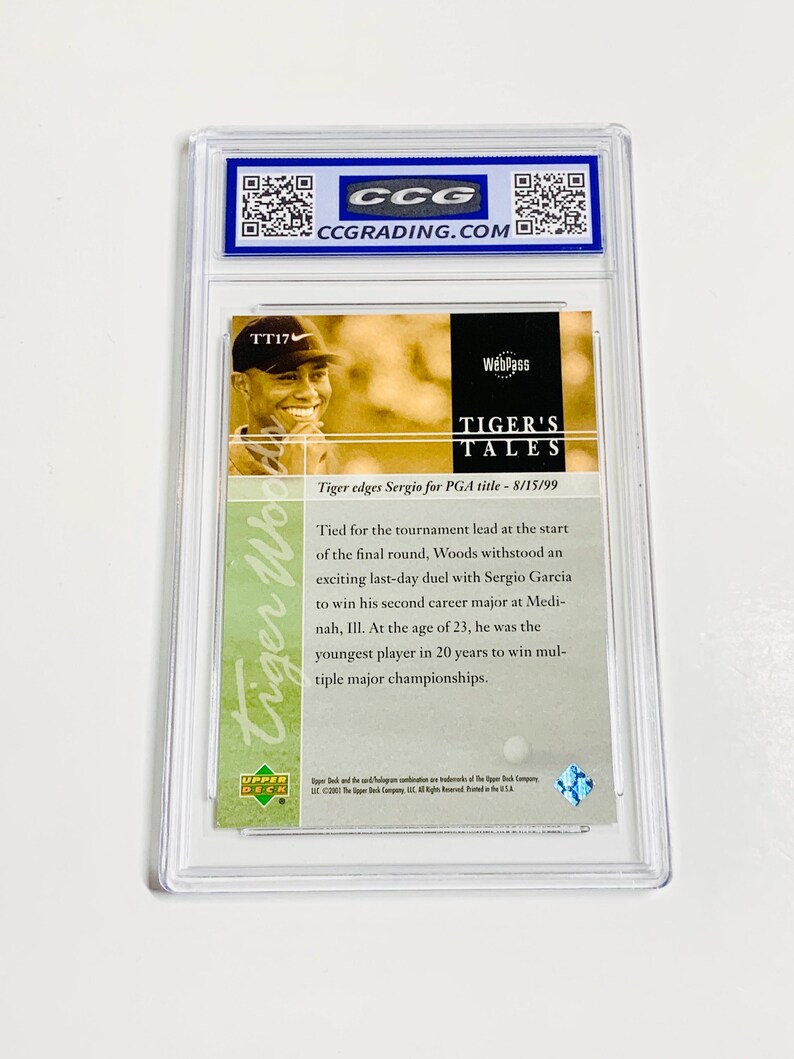 May include: A Tiger Woods trading card encased in a clear plastic holder. The card features a photo of Tiger Woods and text that reads "TIGER'S TALES" and "Tiger edges Sergio for PGA title - 8/15/99". The card is graded by CCG.