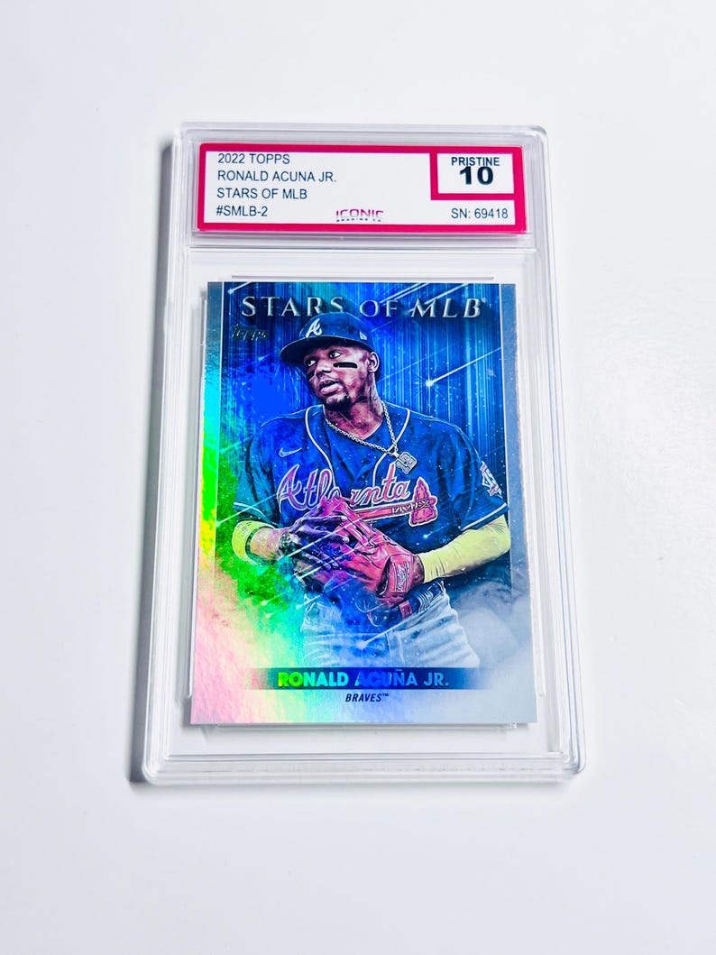 May include: A baseball card featuring Ronald Acu&ntilde;a Jr. of the Atlanta Braves, from the 2022 Topps Stars of MLB series. The card is graded Pristine 10 and encased in a clear protective holder. The card has a holographic design with the player in action.