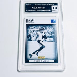 Könnte beinhalten: Eine bewertete Sport-Sammelkarte mit Malik Nabers in einer Schwarz-Weiß-Aufnahme. Die Karte ist mit "2024 Panini Instant NFL" und "Black and White Rookies" beschriftet. Die Karte ist in einem transparenten Schutzhalter eingeschlossen.