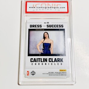 May include: A Caitlin Clark trading card, encased in a clear protective holder. The card features a photo of Clark in a blue dress, with the text "DRESS FOR SUCCESS" and "CAITLIN CLARK CHRONICLED". The card is from the 2025 Panini WNBA series.