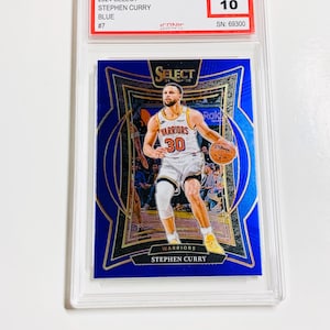 Pode incluir: Um cartão de basquete azul 2024 Select Stephen Curry, classificado como Pristine 10, em um suporte protetor. O cartão apresenta Curry com seu uniforme Warriors, com uma bola de basquete. O número de série do cartão é 69300.