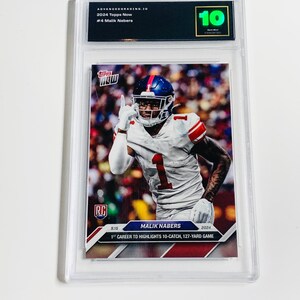 Könnte beinhalten: Eine bewertete 2024 Topps Now Sammelkarte mit Malik Nabers im Giants-Trikot. Die Karte ist in einer transparenten Schutzhülle eingeschlossen und mit 10 bewertet. Die Karte zeigt Nabers' ersten Touchdown mit 10 Catches und einem 127-Yard-Spiel.