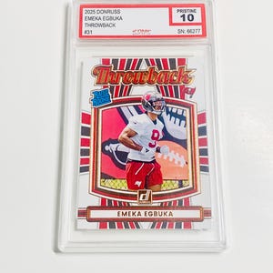 May include: A graded sports trading card featuring Emeaka Egbuka in a football uniform. The card is labeled "Throwback" and "Rated Rookie." The card is encased in a clear protective holder, with a "Pristine 10" grade.